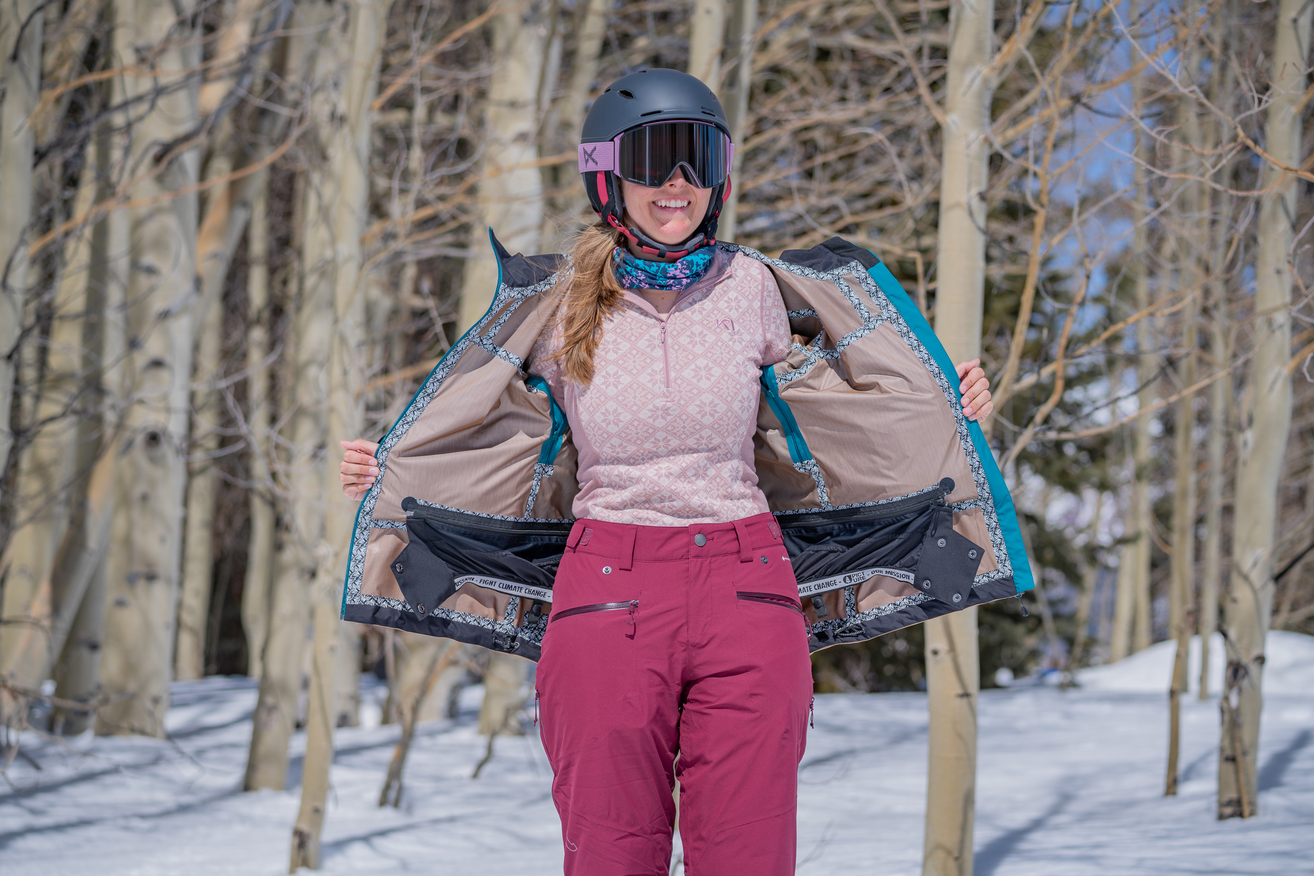 A woman pulling open her outer ski shell to reveal the base layer underneath.