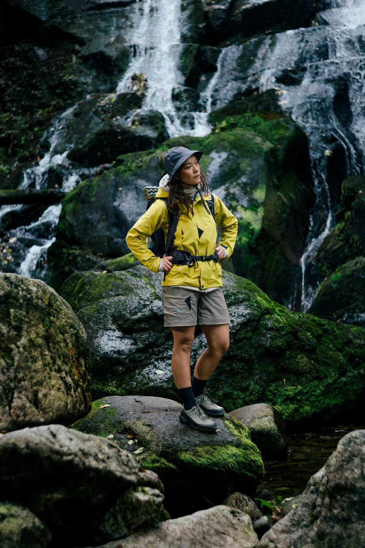 A hiker wearing a Klättermusen waterproof jacket standing near a waterfall.