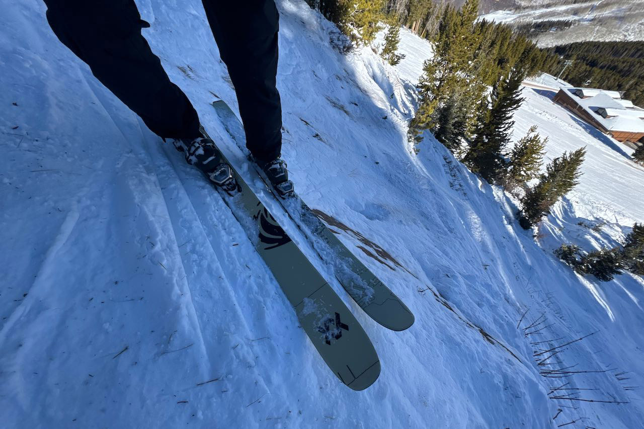 A pair of Völkl Revolt skis standing upright in the snow next to ski poles.