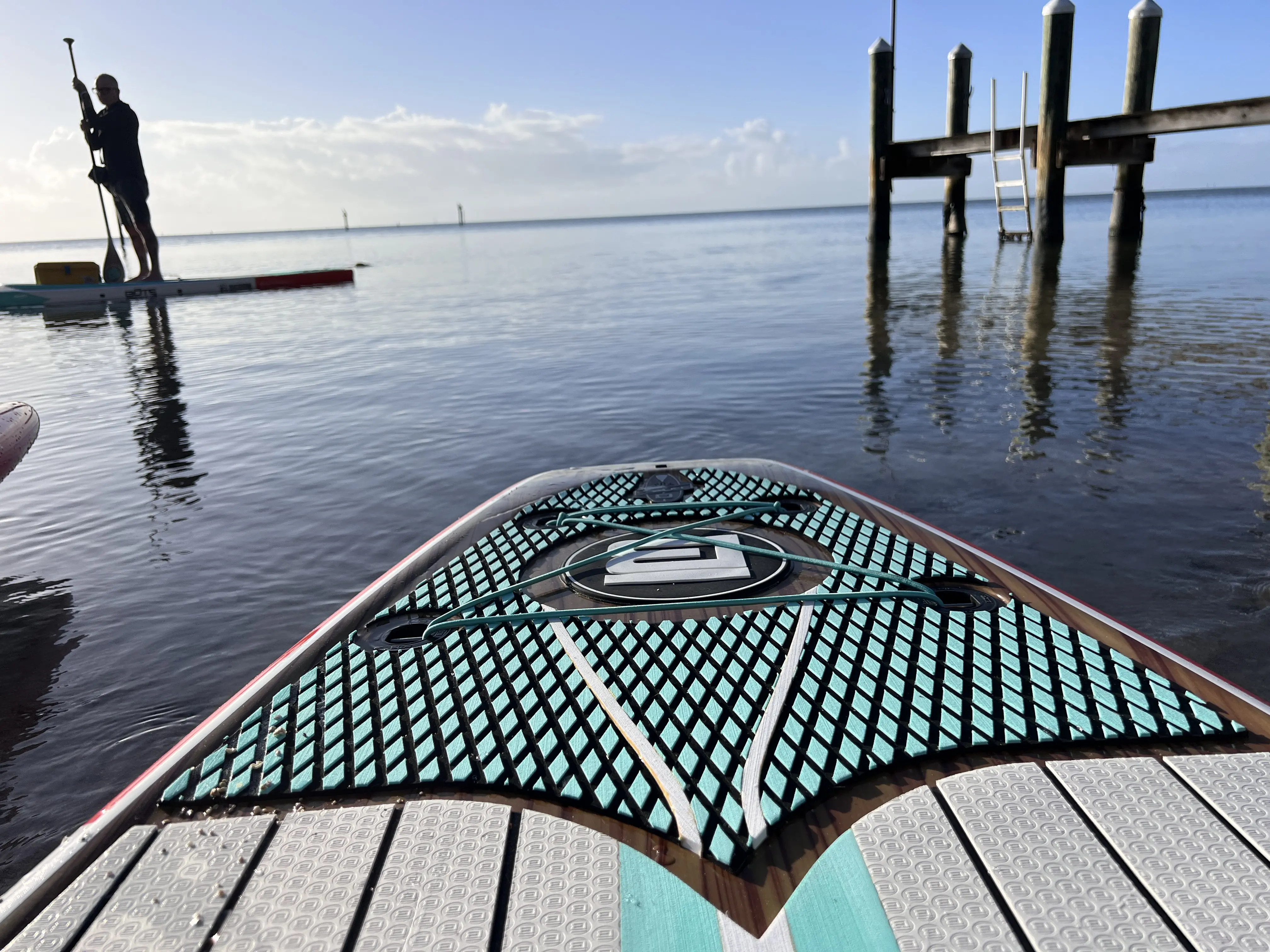 A dry bag secured by bungee cords on the front deck of a hard paddleboard.