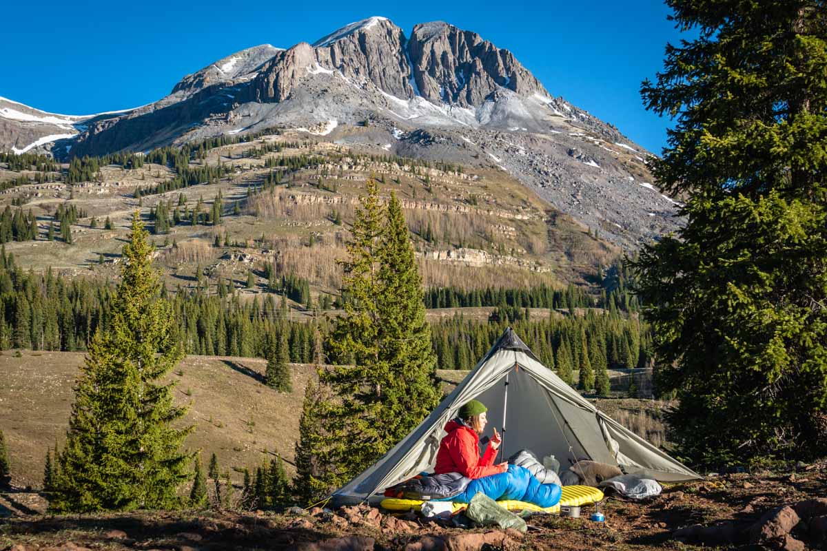 A person sitting up in a sleeping bag looking at the mountains on a cool morning.