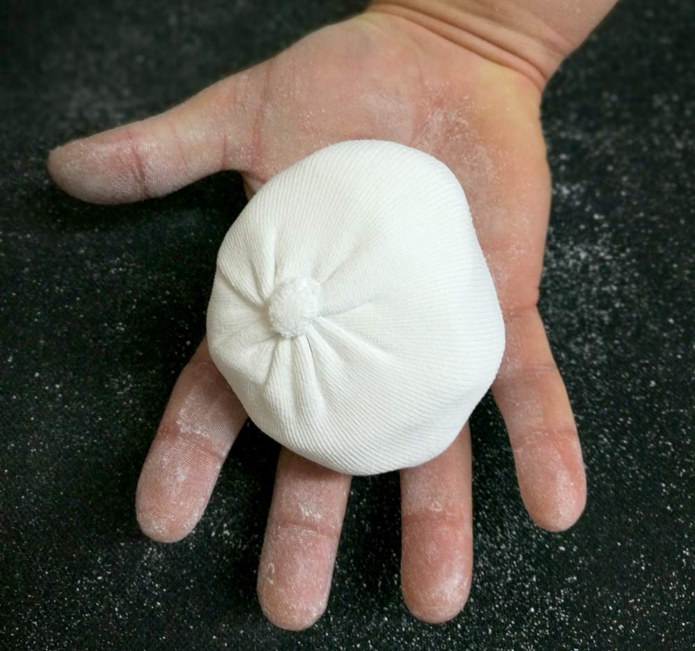 An open palm holding a mesh climbing chalk ball filled with white powder