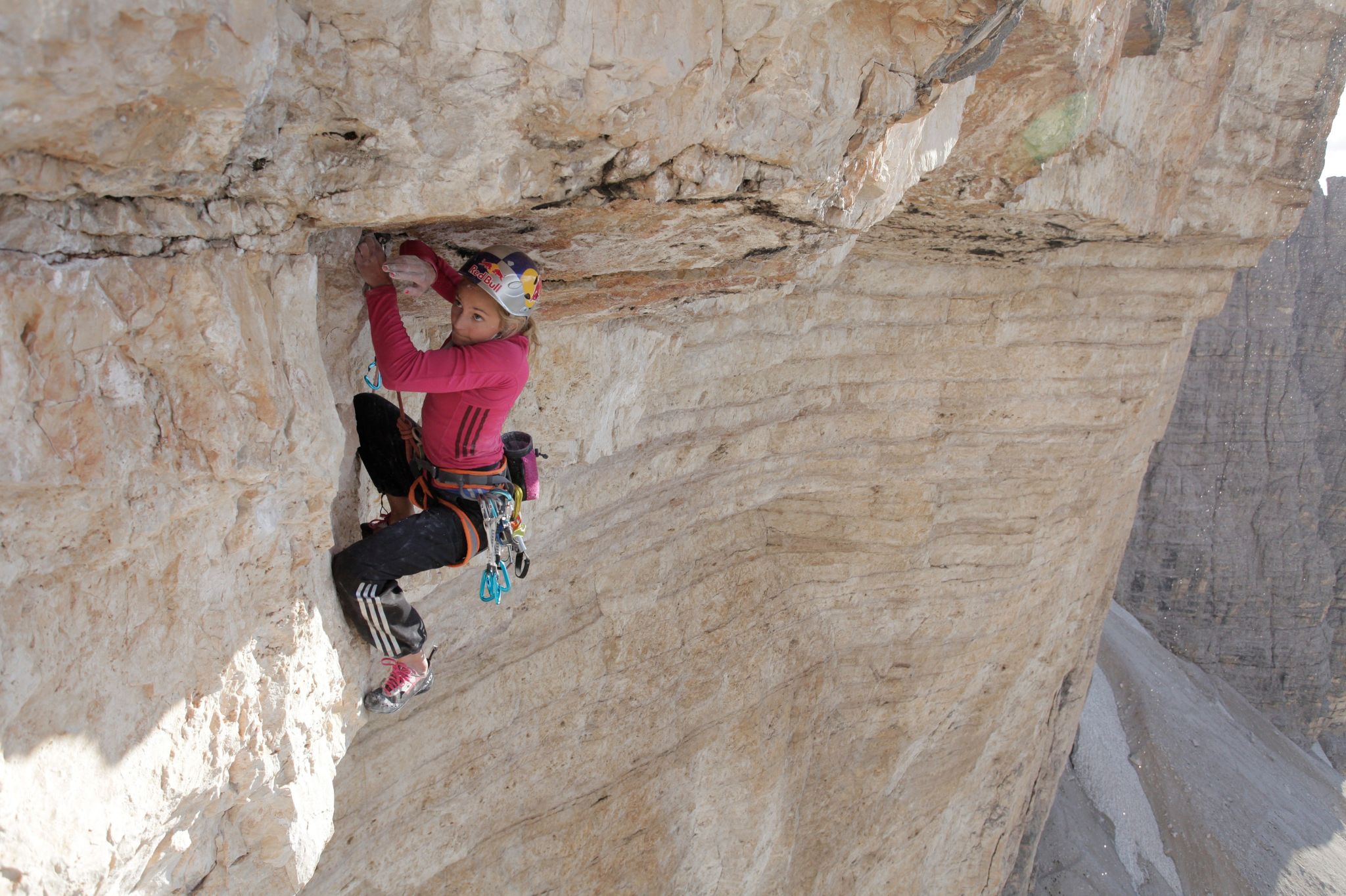 A female climber moves through a steep roof section of an outdoor rock face.