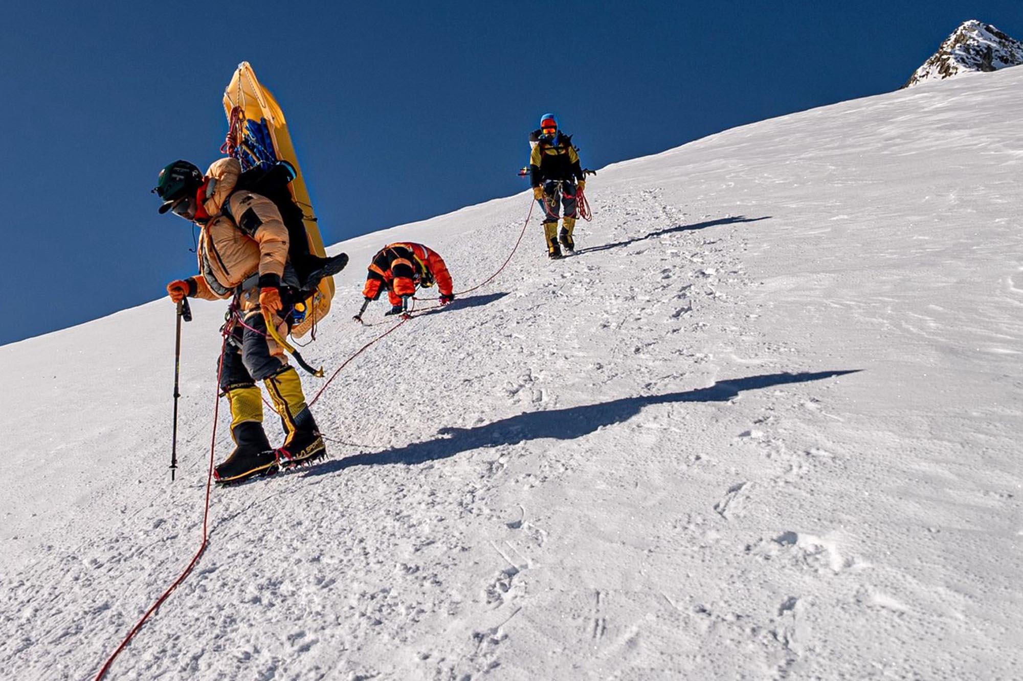 Hari Budha Magar crawling upward on a steep, snow-covered mountain face using his arms and prosthetics.