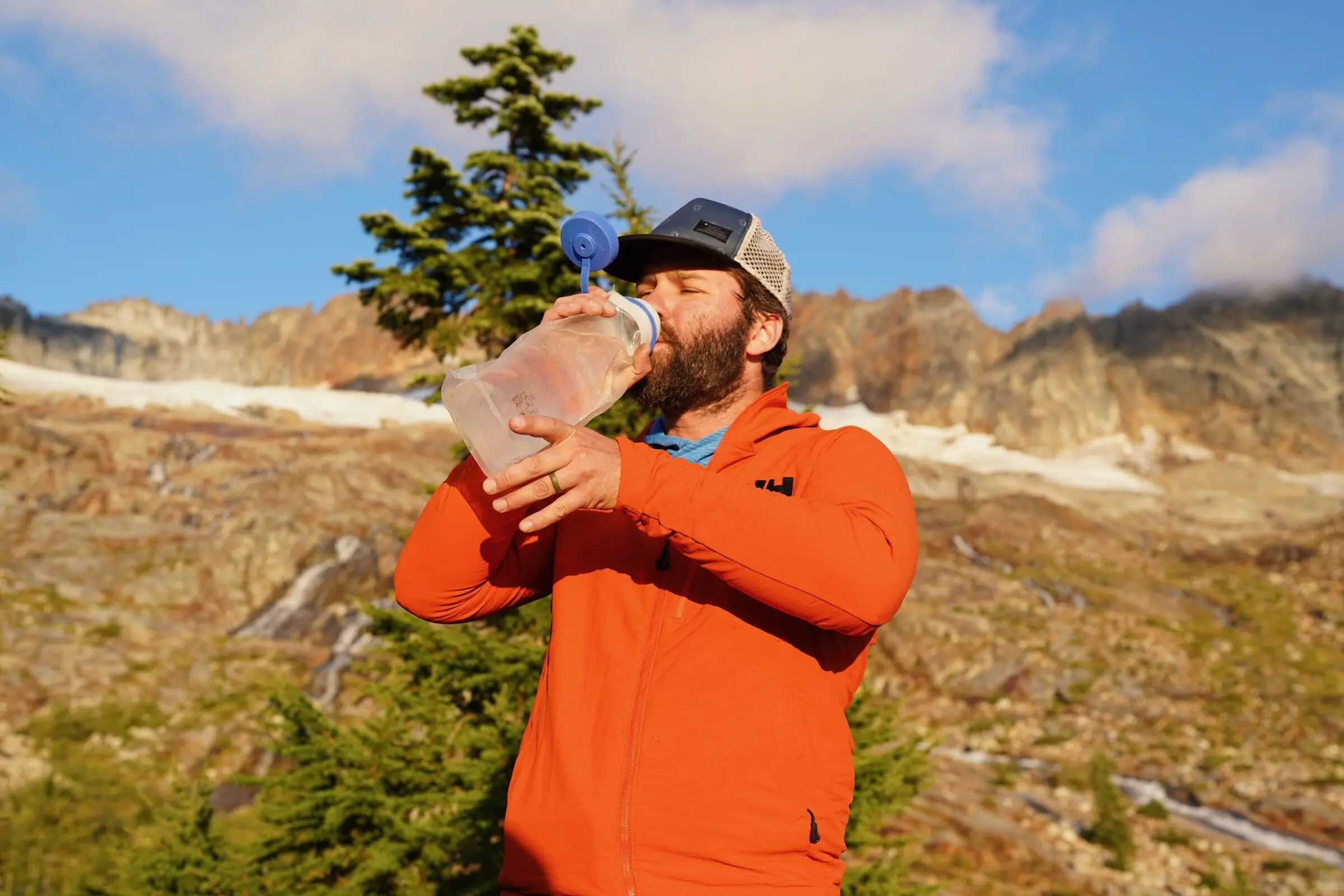 A person filtering water into a bottle while sitting on a rocky riverbank