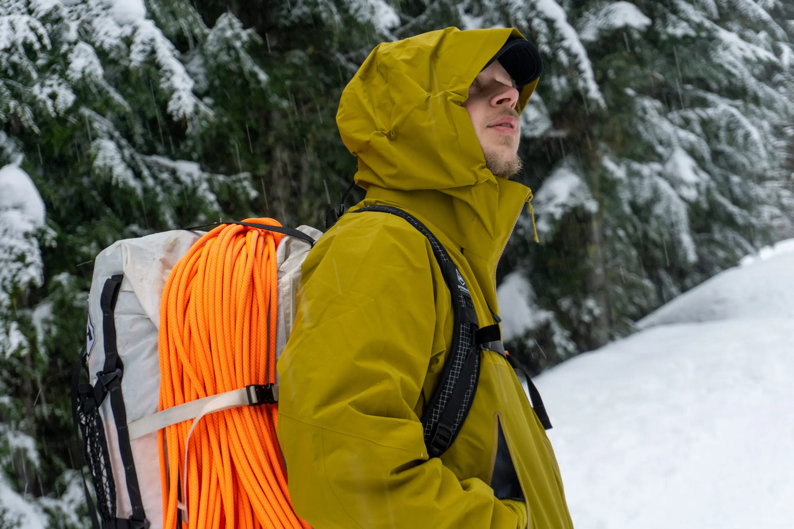 A hiker wearing a technical hardshell jacket in snowy, high-altitude mountain conditions.