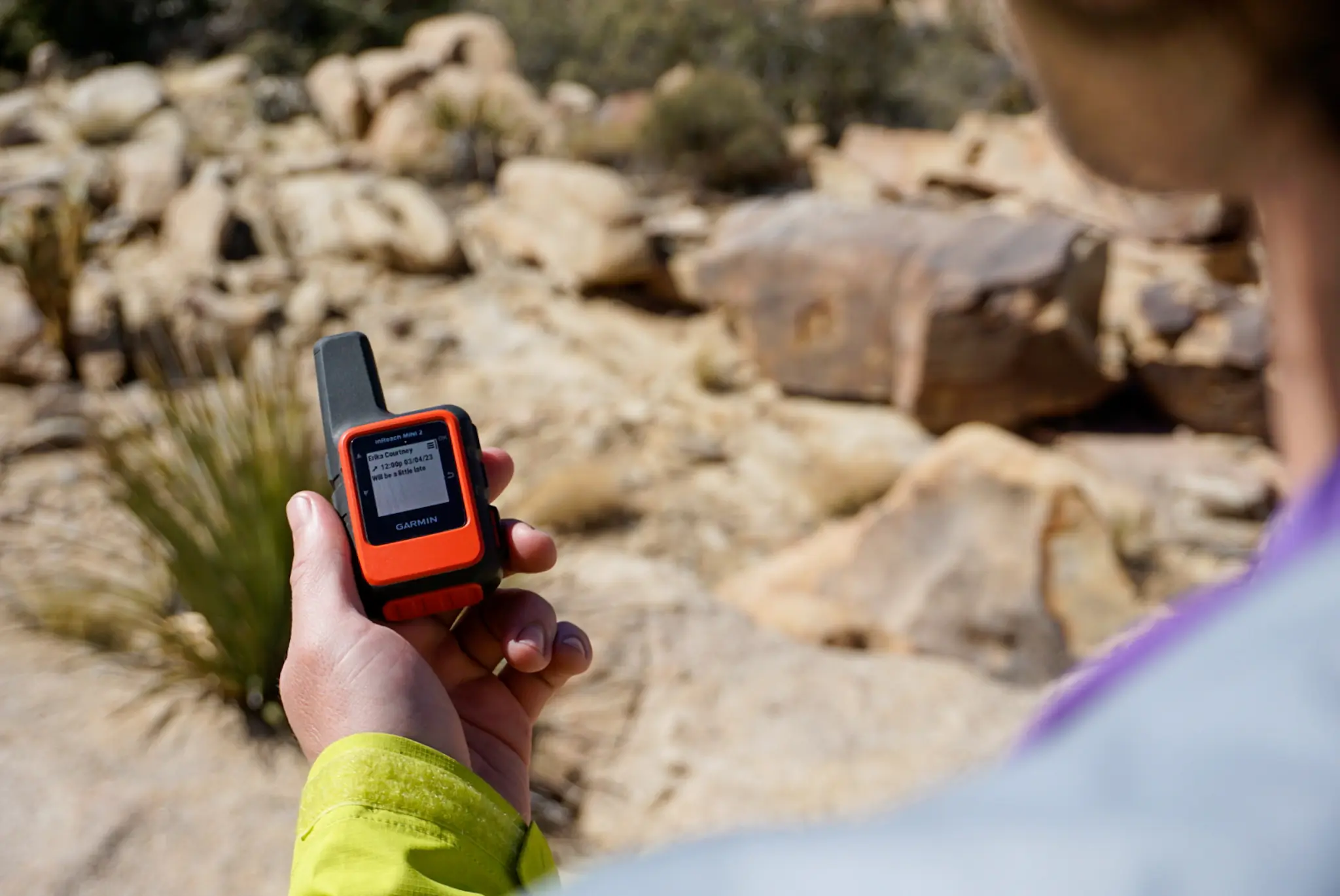 A hand holding the Garmin inReach Mini 2 against a background of Joshua Tree National Park.