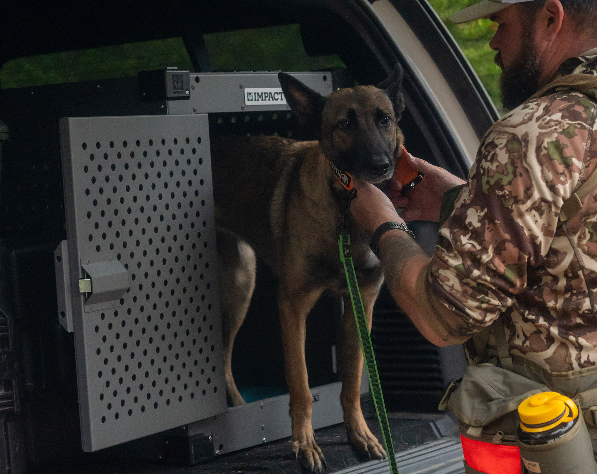 A hunter in orange gear standing with his dog next to an Impact Dog Crate.