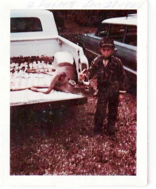 Black and white vintage photograph of a child with a buck in a forest clearing.