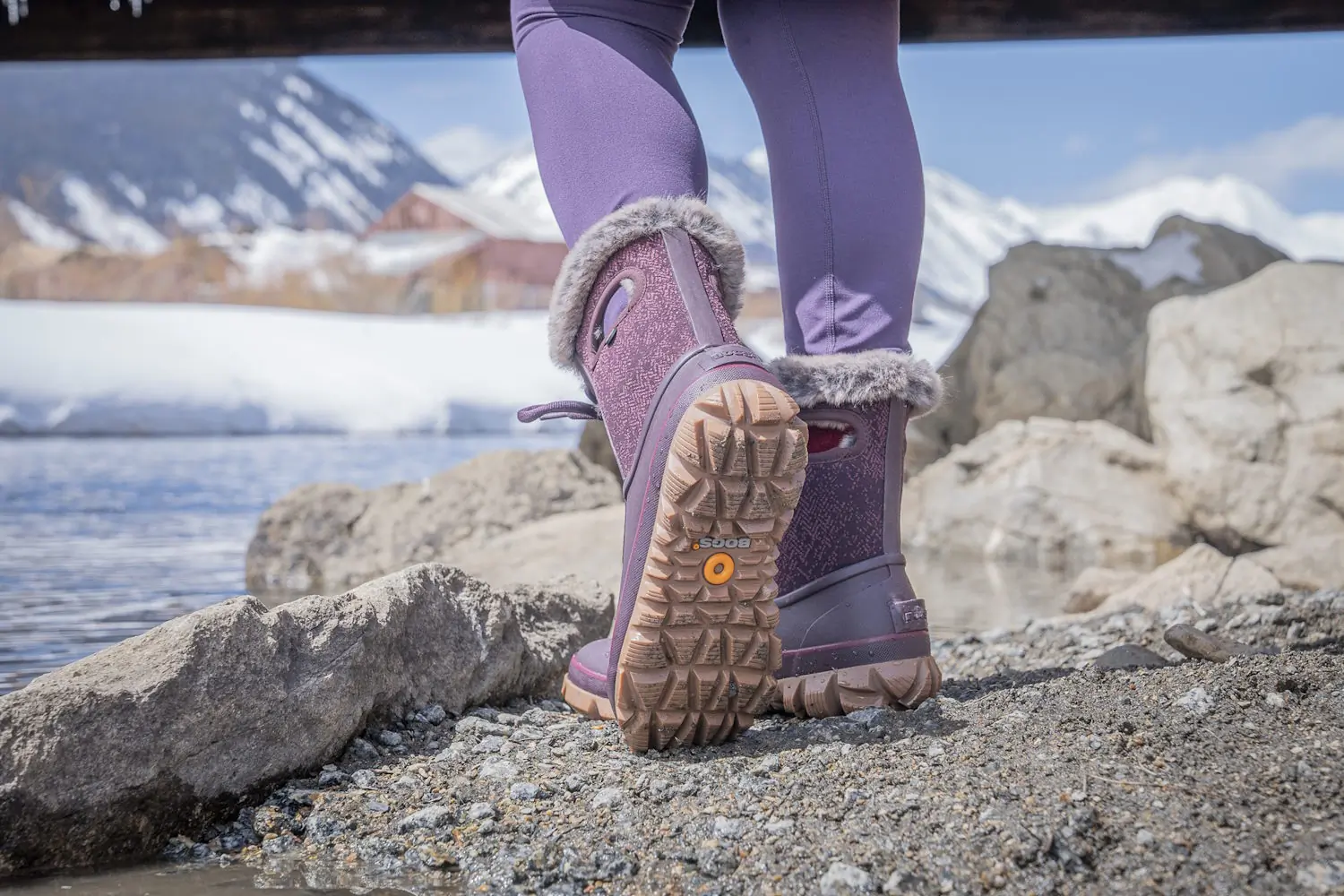 Close-up of Bogs boots on rocky, snow-dusted ground showing the thick rubber outsole.