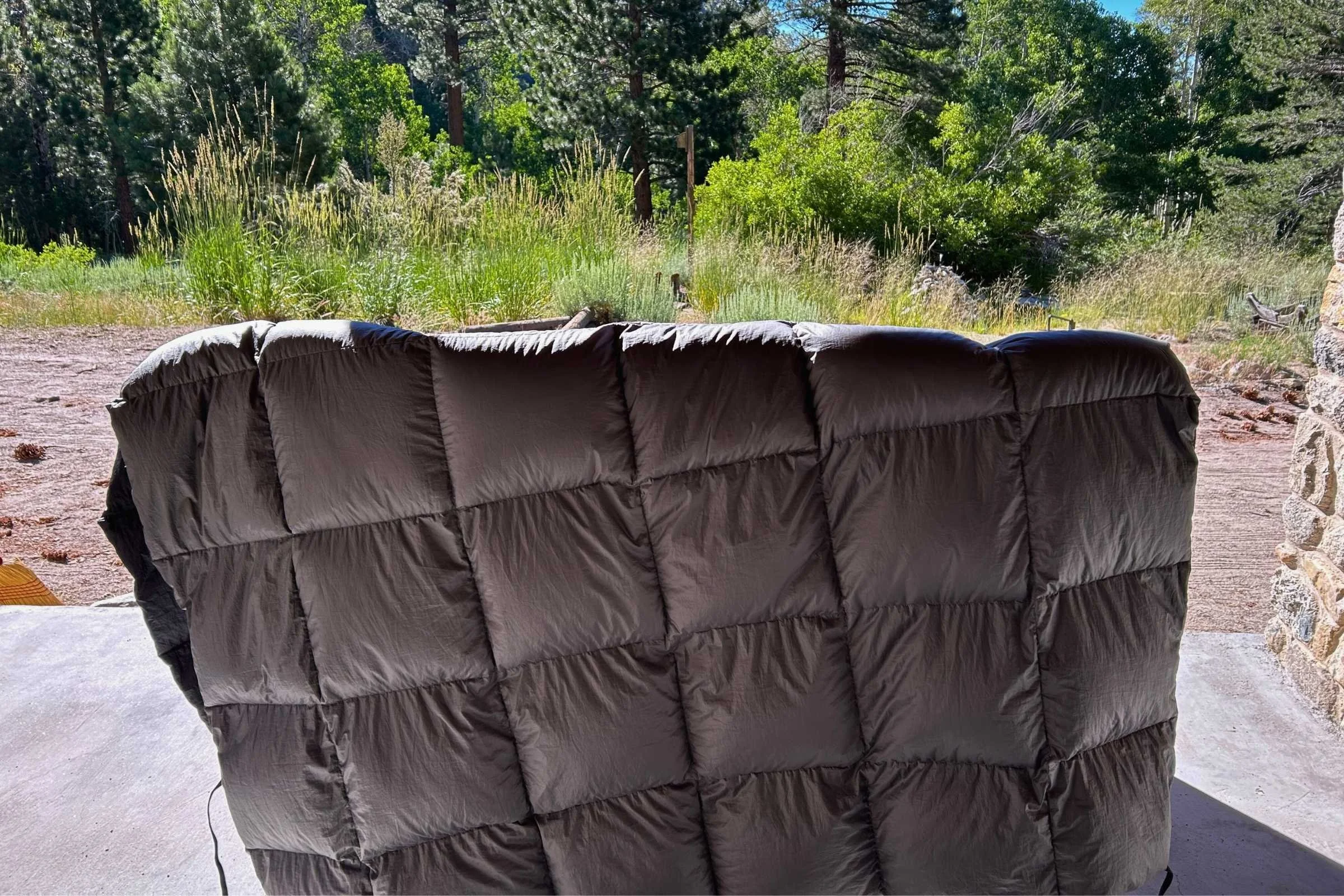 A high-loft down camping comforter drying on a cabin porch with a mountain backdrop.