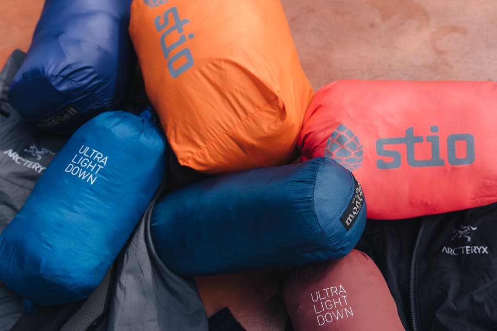Several down jackets compressed into small, colorful stuff sacks.