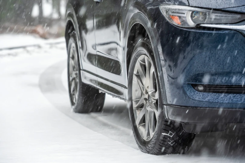 A Mazda CX-5 equipped with Nokian winter tires parked on a snow-covered road in a dense evergreen forest.