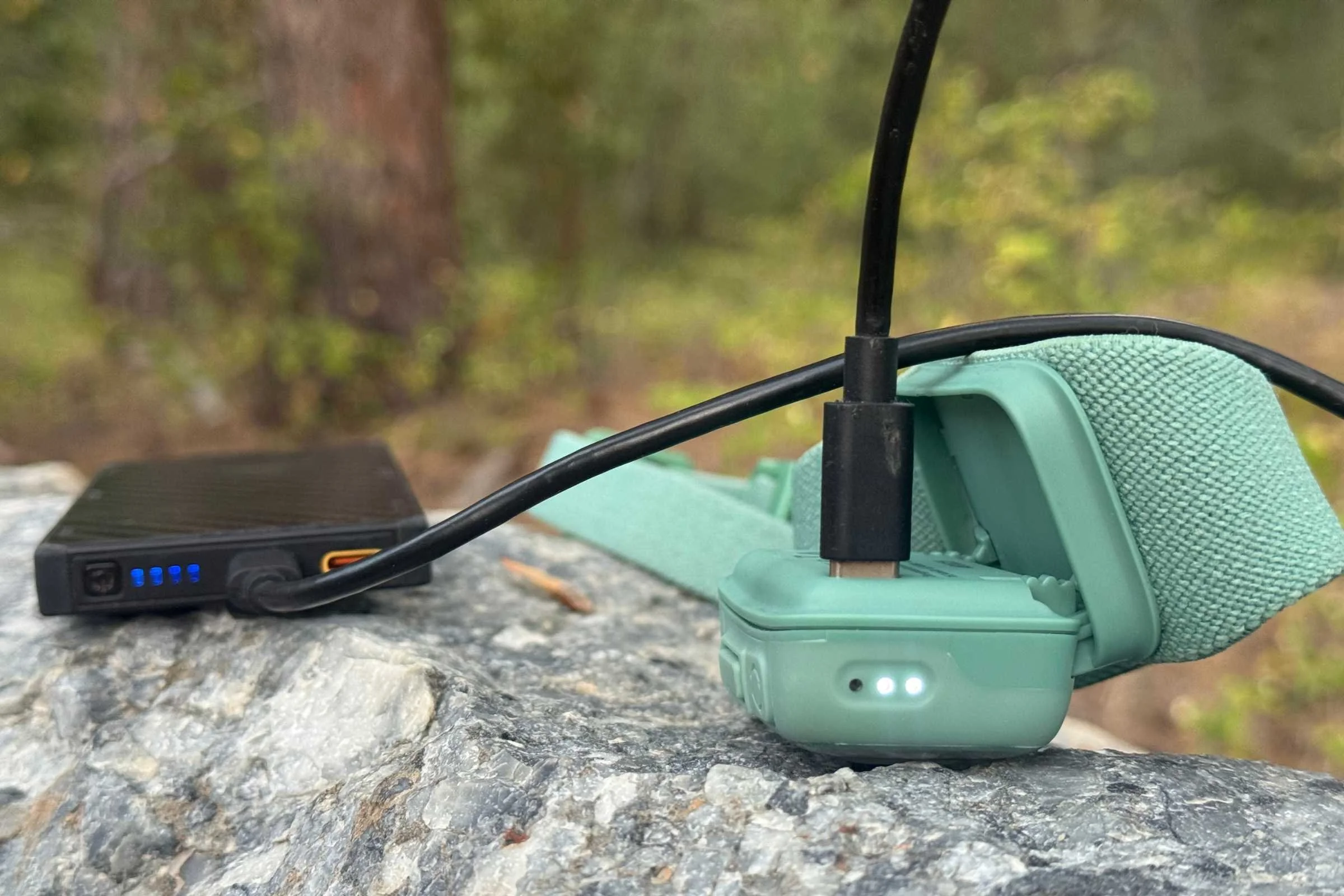 A modern headlamp connected via a USB-C cable to a portable power bank in the field.