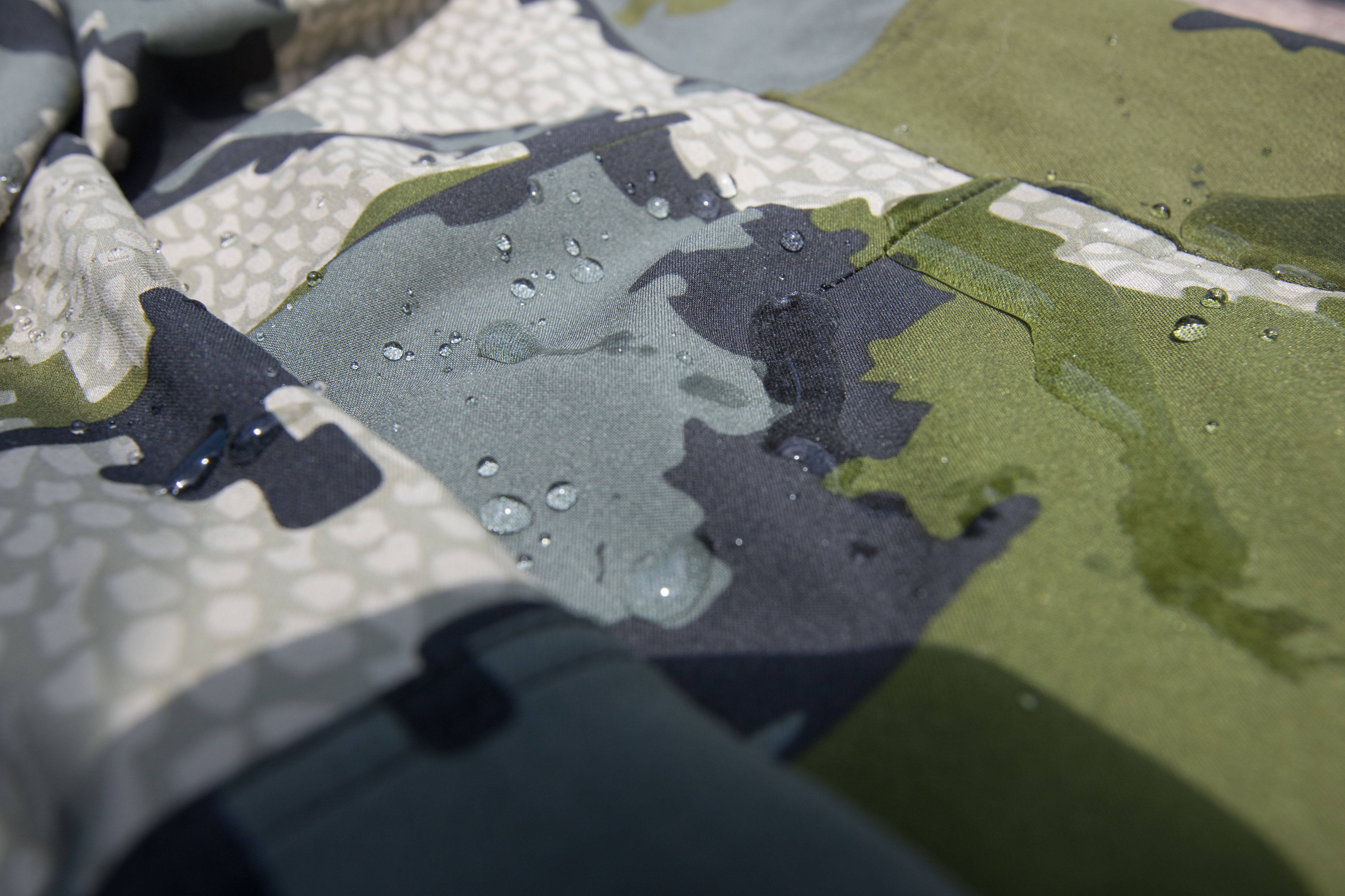 Water droplets beading up and rolling off the surface of camouflage hunting fabric.