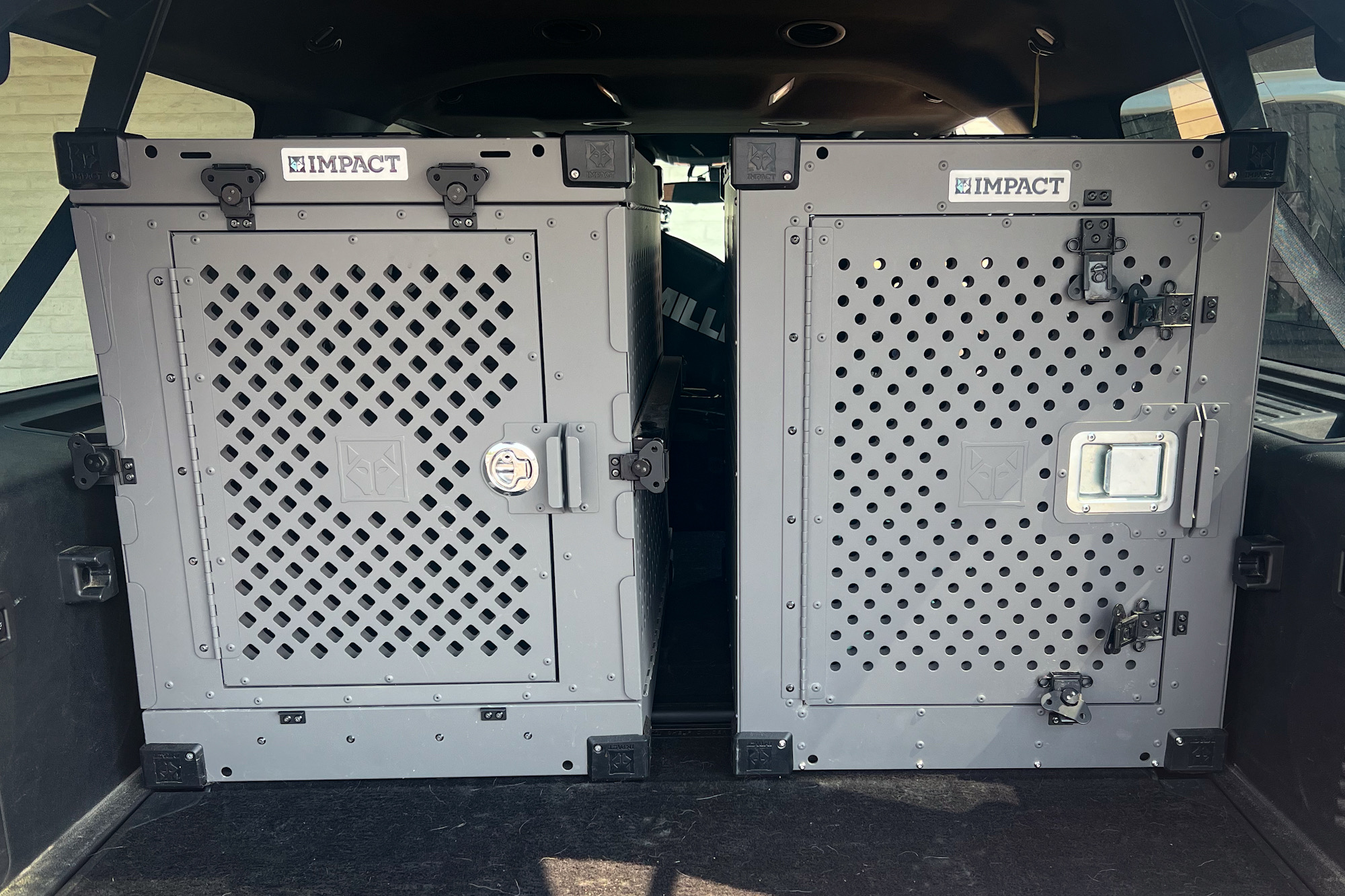 Two silver Impact dog crates installed side-by-side in the cargo area of an SUV.