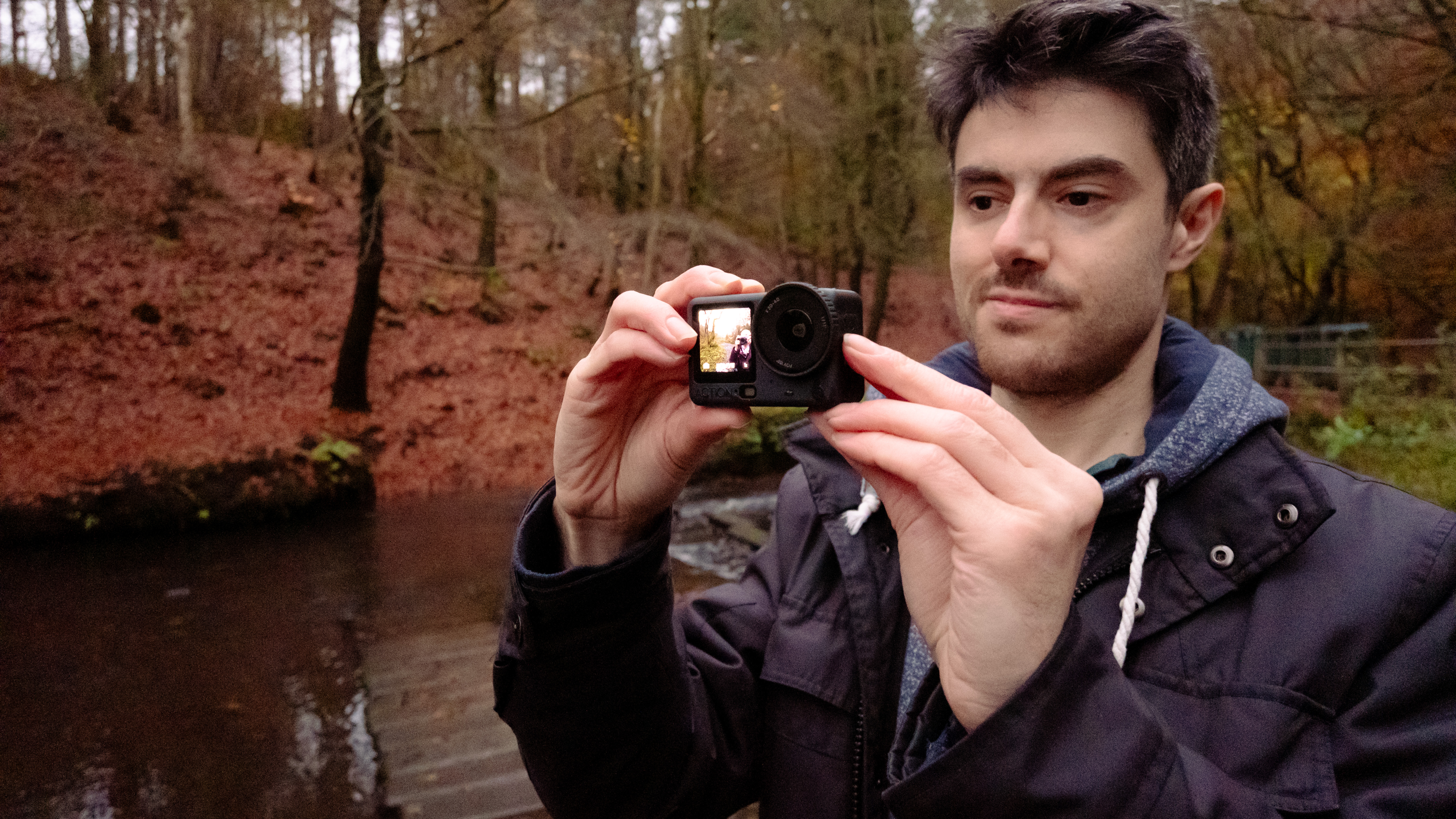 A person holding a DJI Osmo Action camera while hiking in a wooded area.