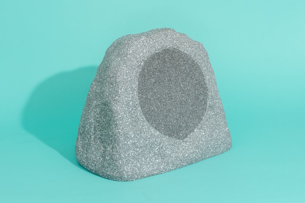 An OSD Audio rock-shaped speaker blending into a garden landscape.