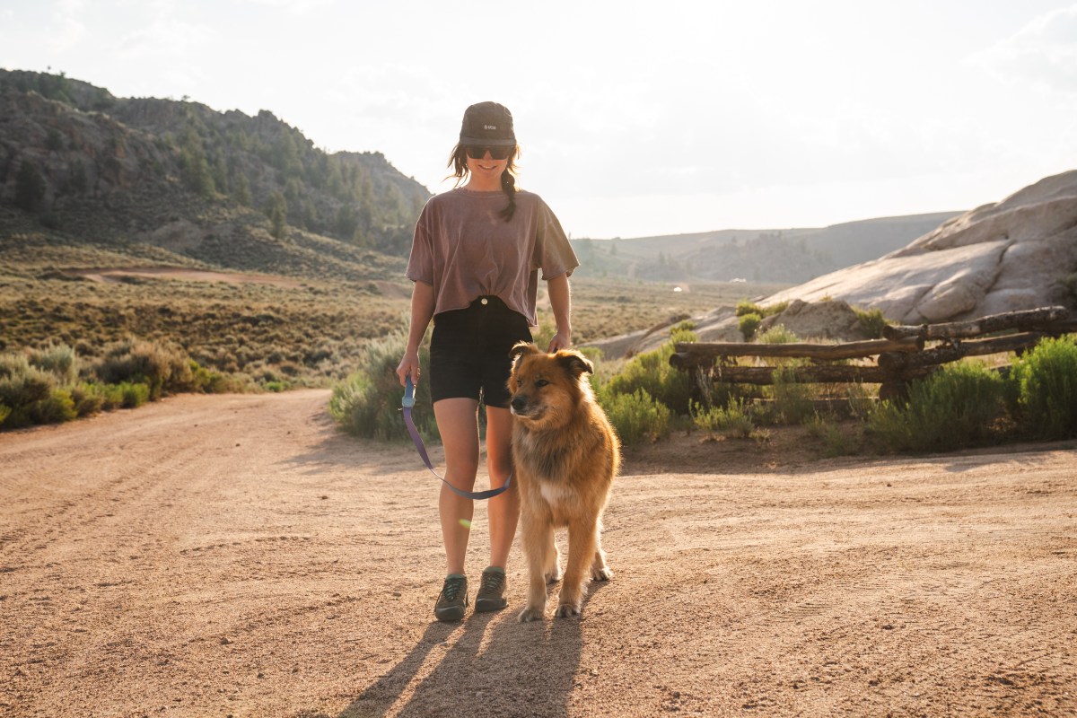 A person walking a dog on a dirt trail using a hands-free belt leash system.