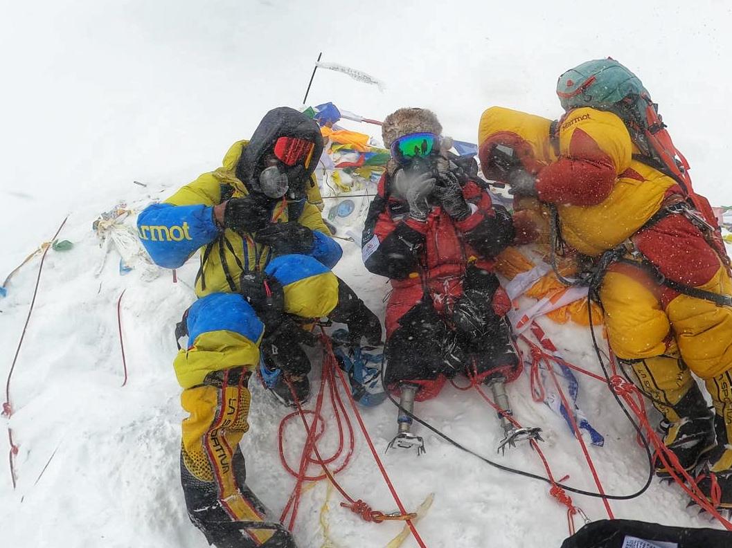 Hari Budha Magar and his support team posing with flags on the crowded summit of Mount Everest.